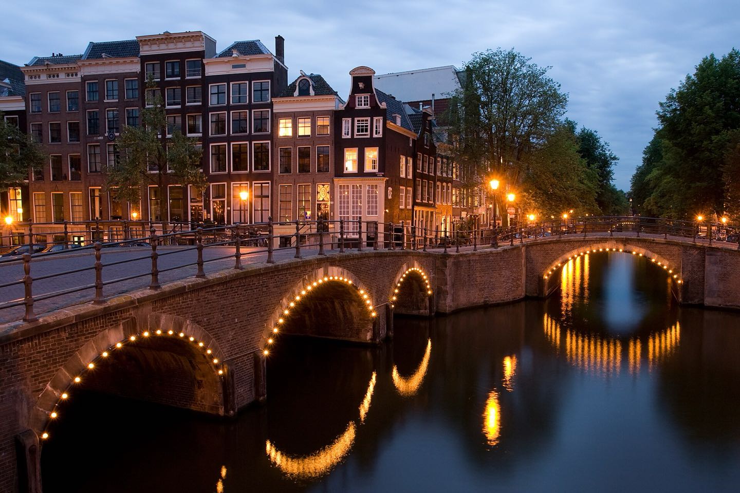 Lit arched bridges where the Reguliersgracht meets the Keizersgracht at dusk