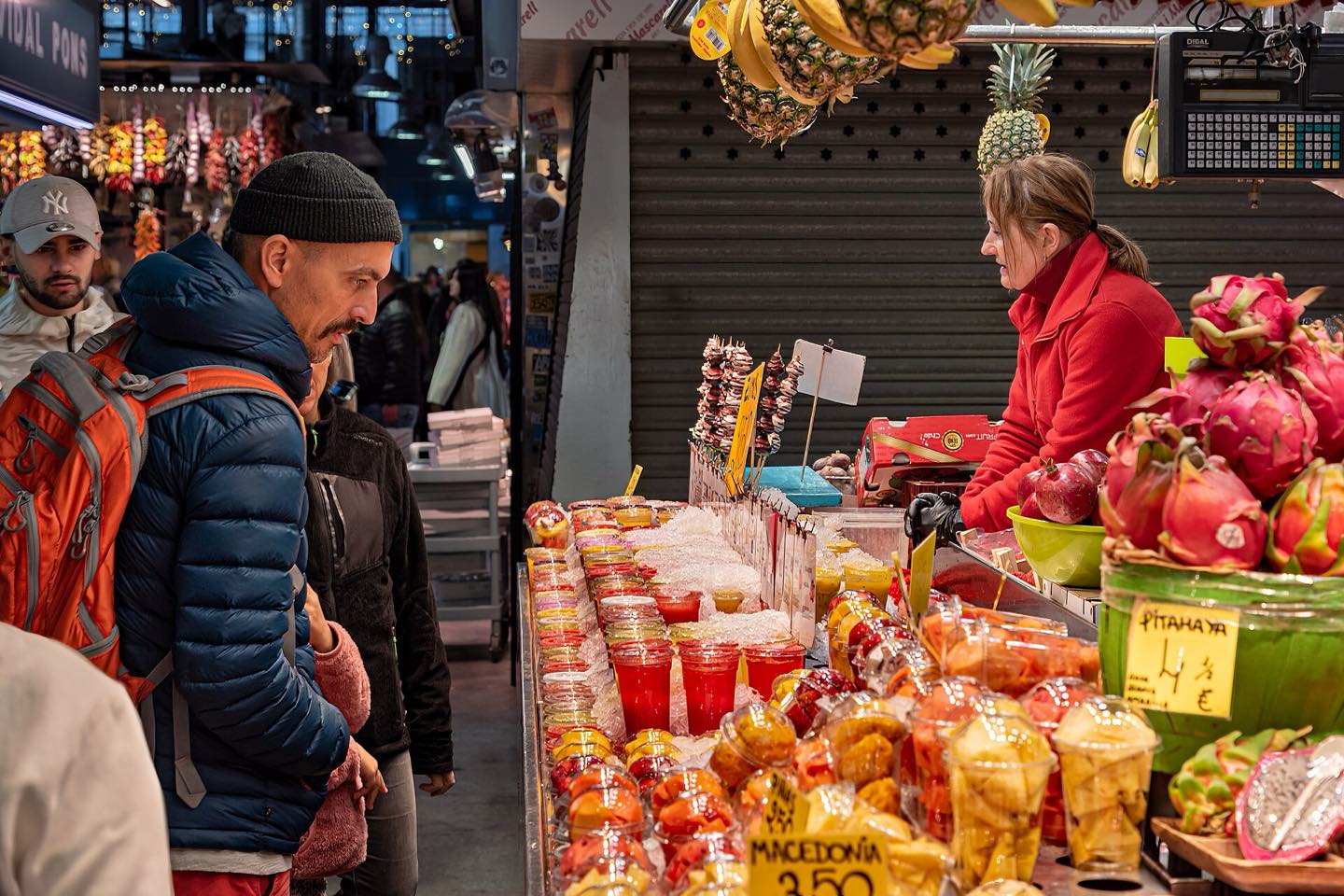 Shoppers at a fruit stall piled with dragon fruit and juices in La Boqueria