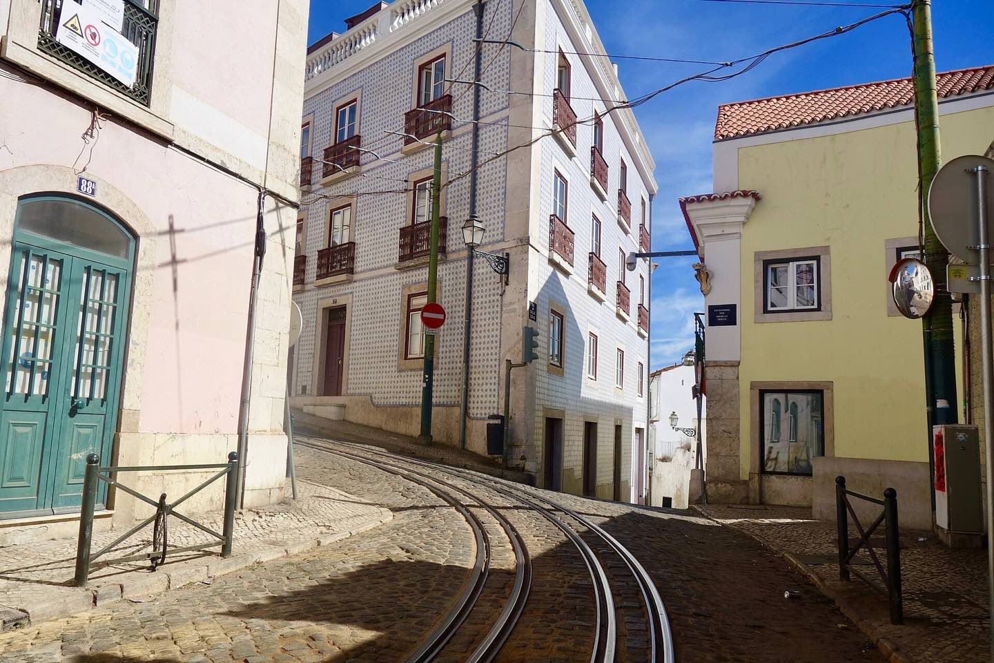 Tram tracks curving through a sunny lane of Alfama, Lisbon