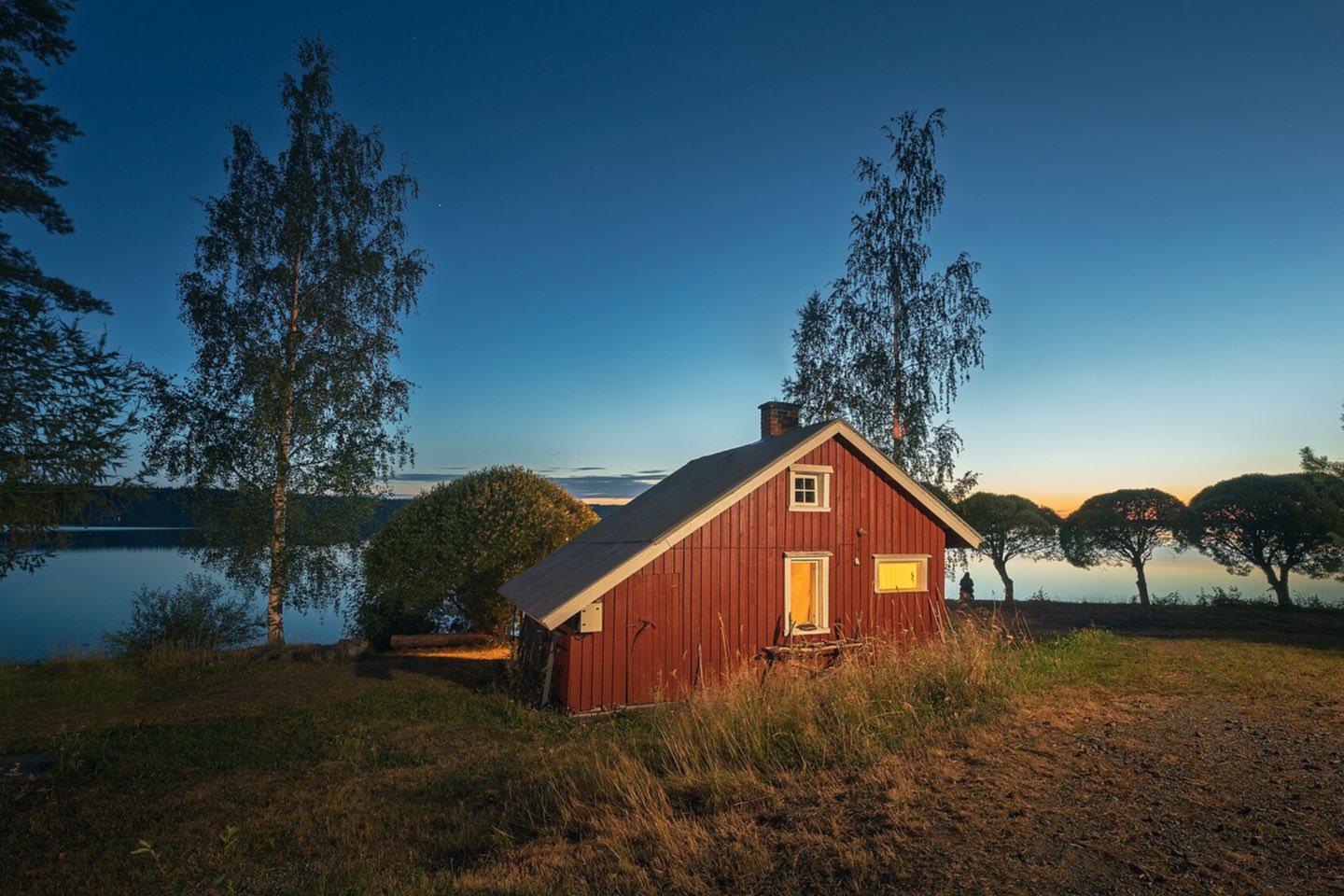 A red wooden sauna cabin glowing at dusk beside a Finnish lake