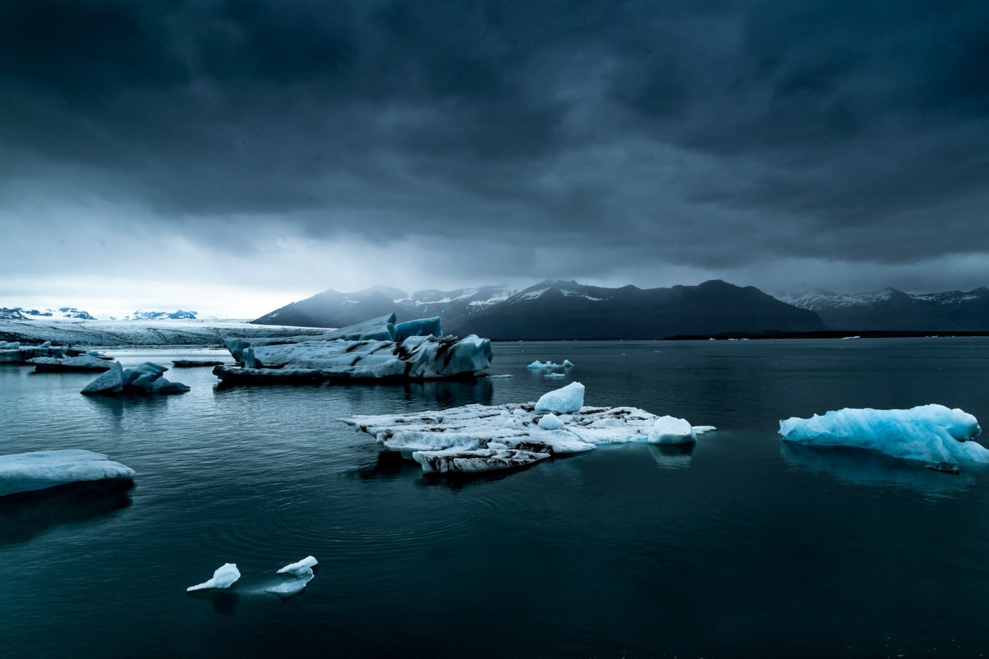 Blue icebergs floating on the dark water of Jökulsárlón under storm clouds