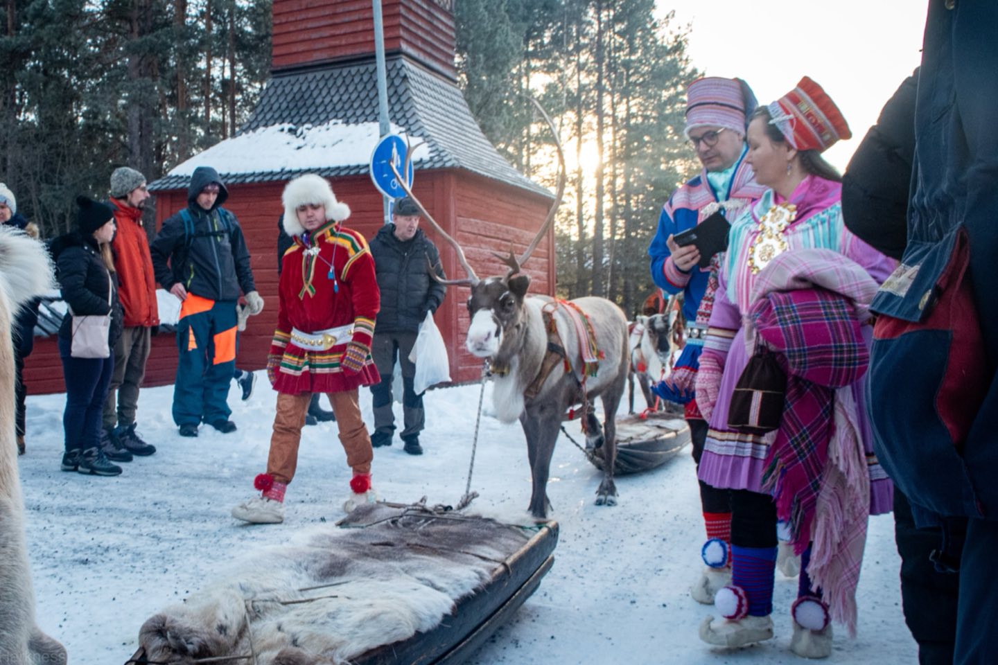 Sámi herders in traditional gákti leading a reindeer through a snowy street