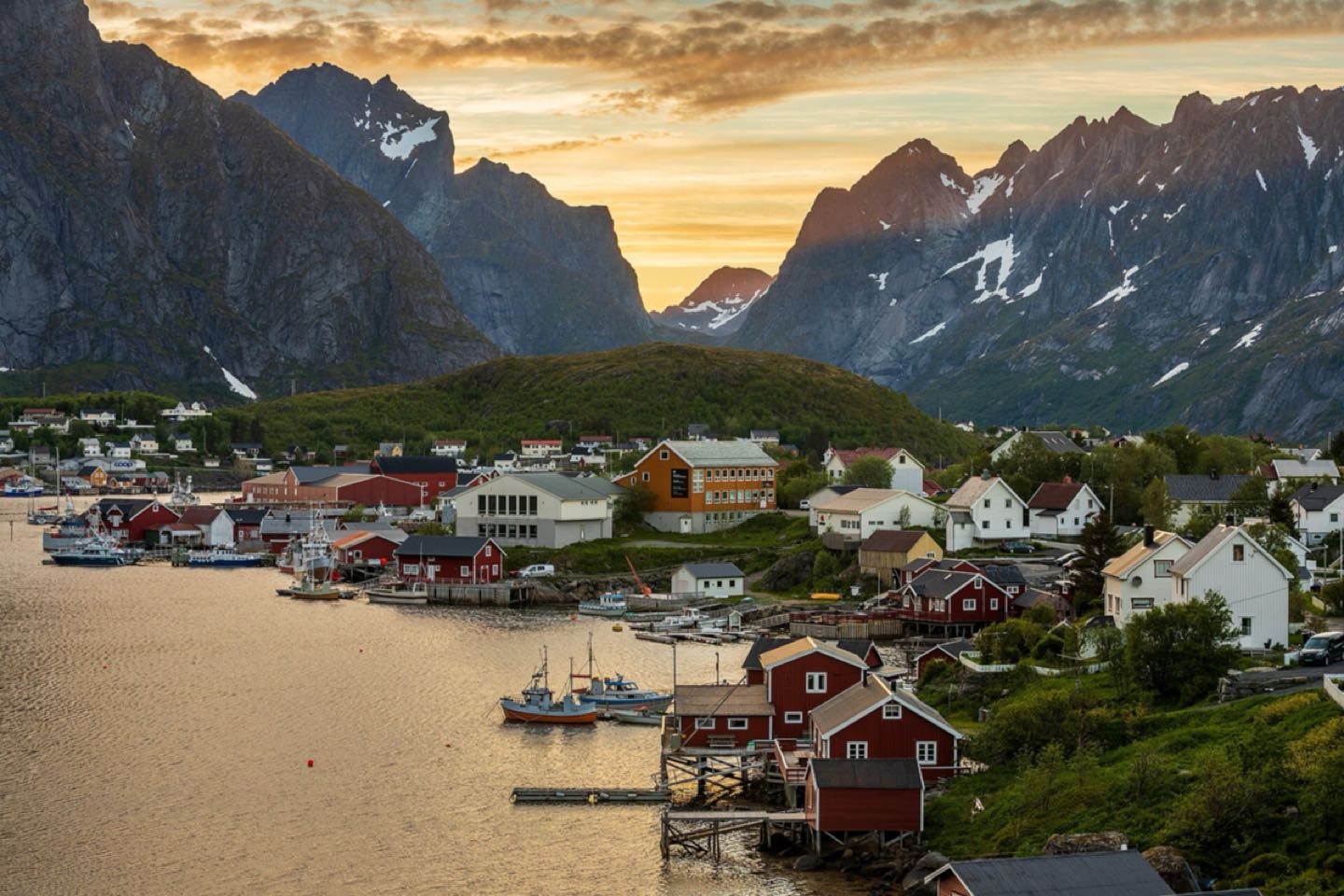 Red fishing cabins and boats in Reine below jagged peaks at sunset