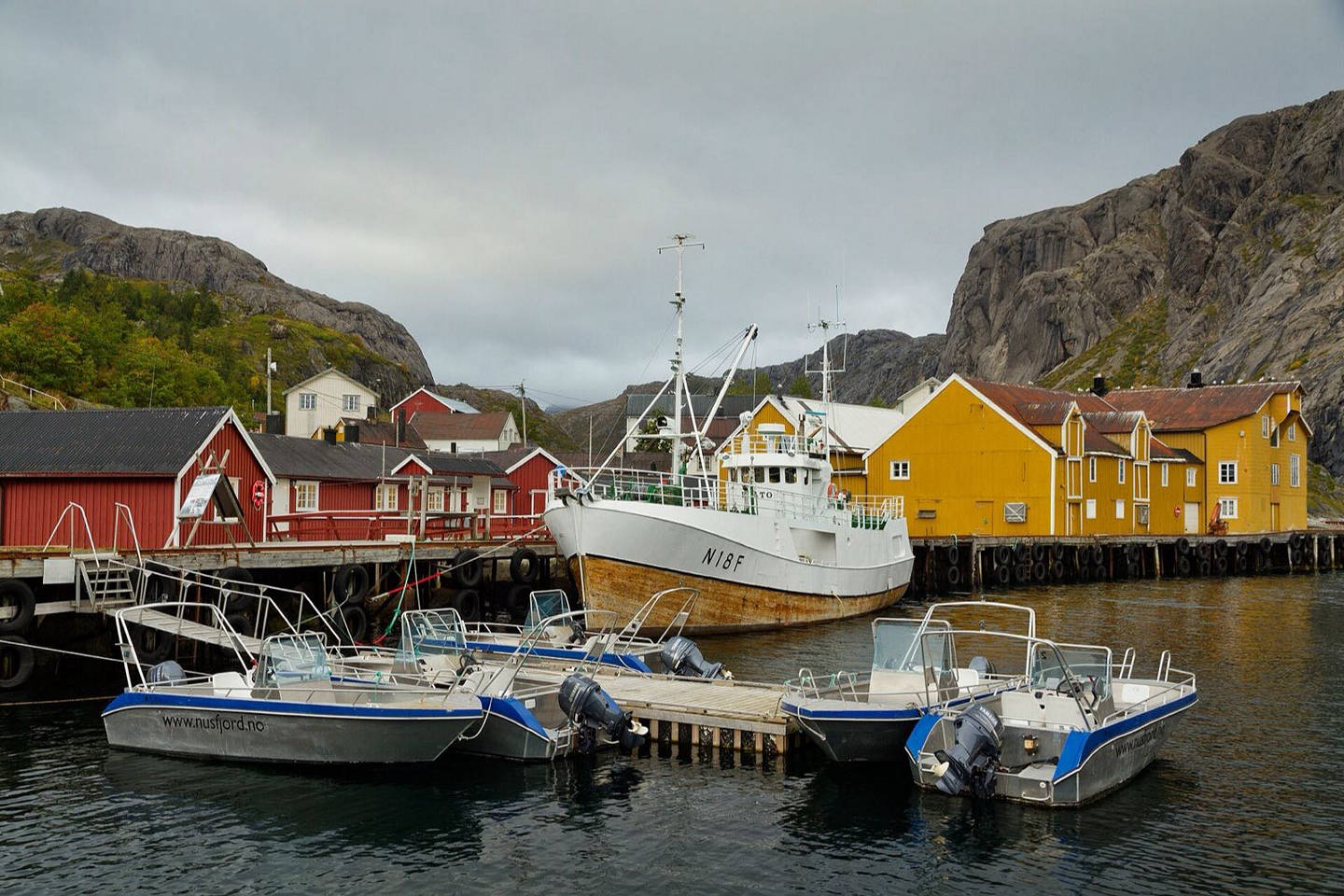 Boats moored among red fishing cabins in Nusfjord, Lofoten