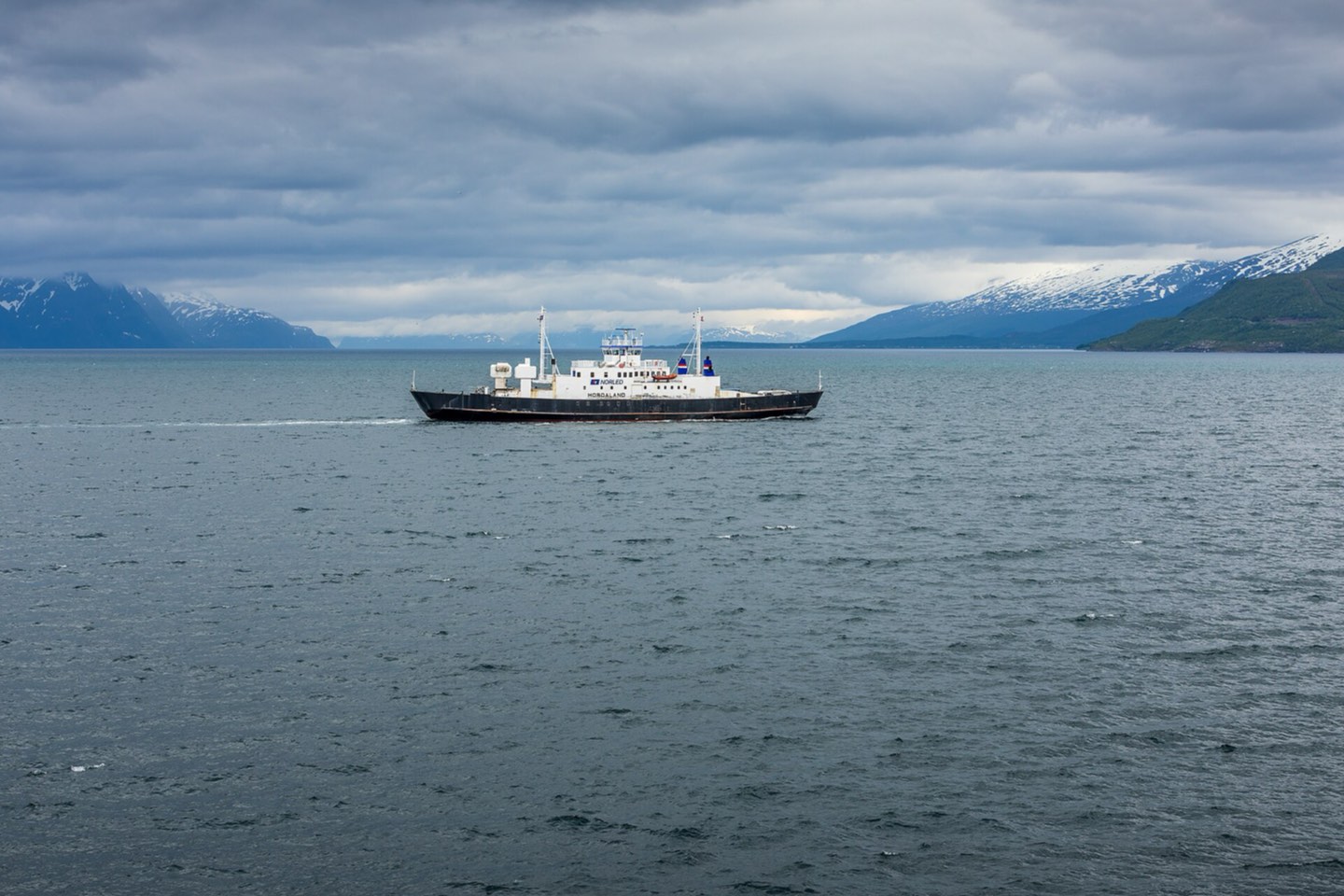 A small car ferry crossing Lyngenfjord beneath snow-capped mountains