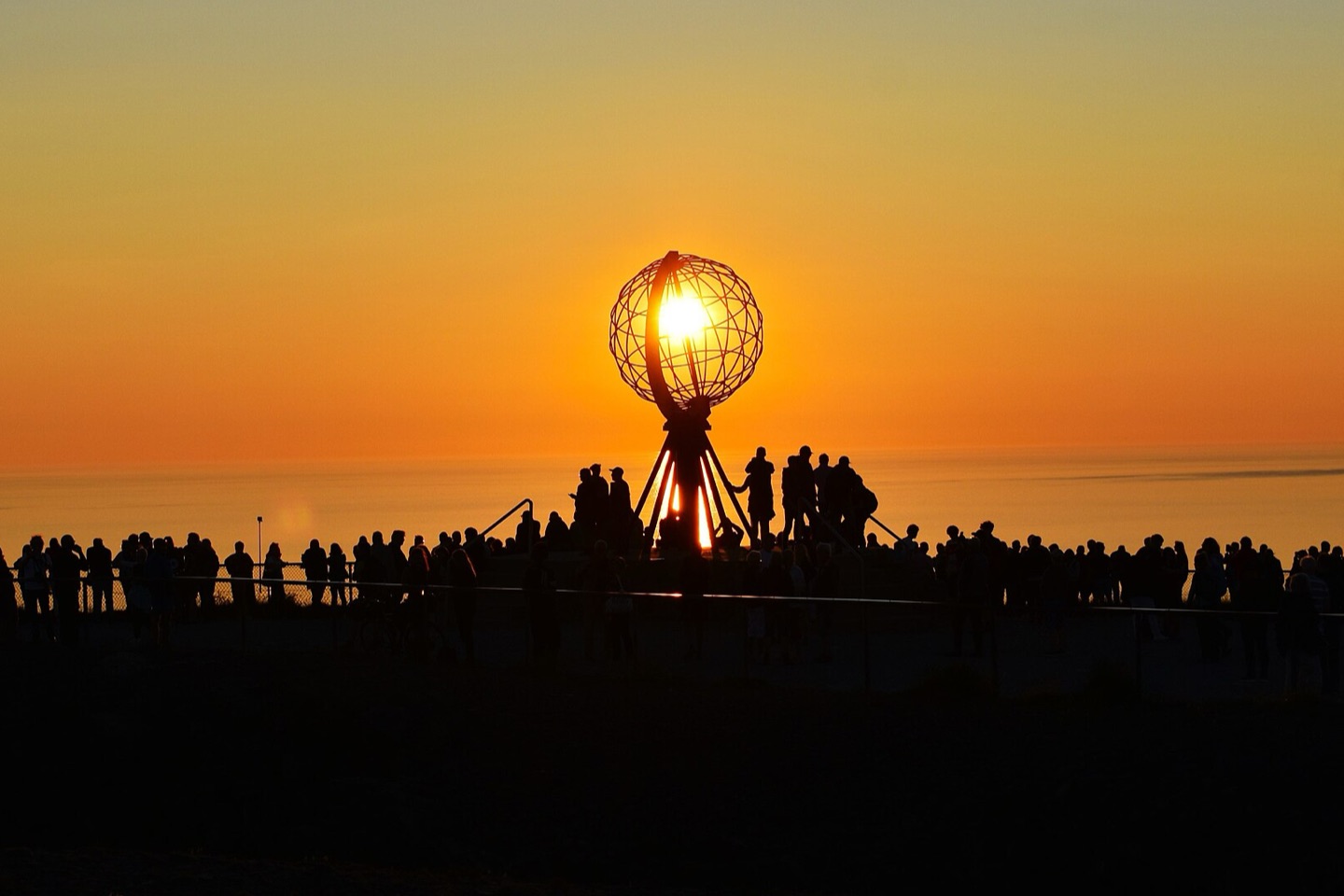 Visitors silhouetted around the globe monument at the North Cape under the midnight sun