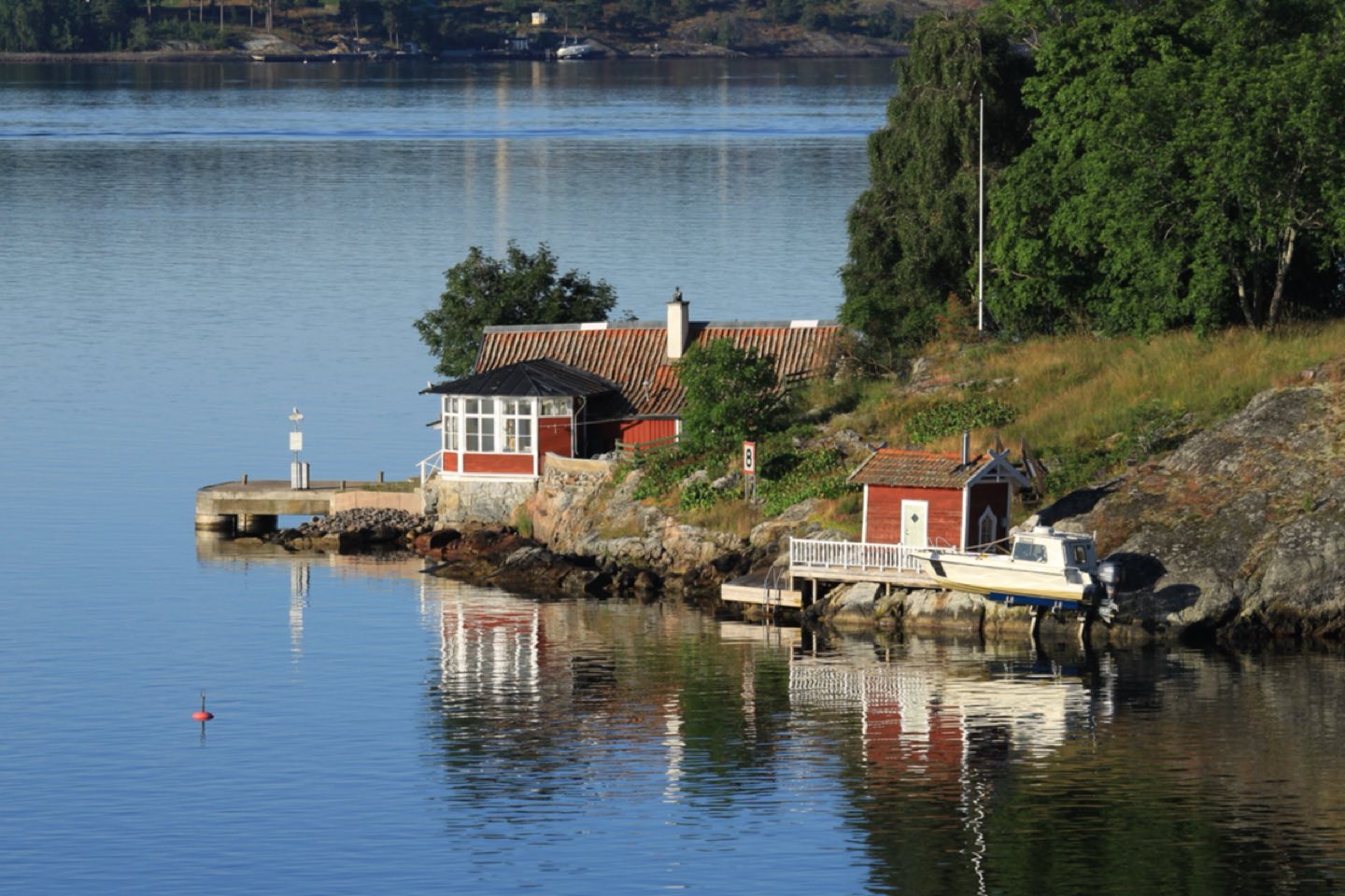 A red wooden summer house and boathouse on a rocky island shore