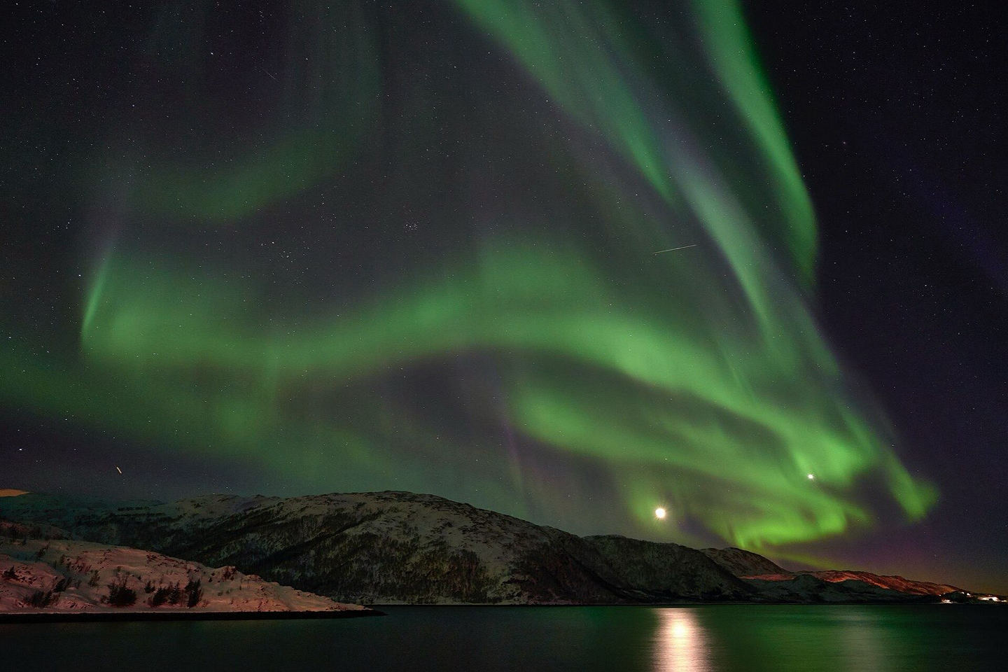 Green northern lights over a snowy shore near Tromsø