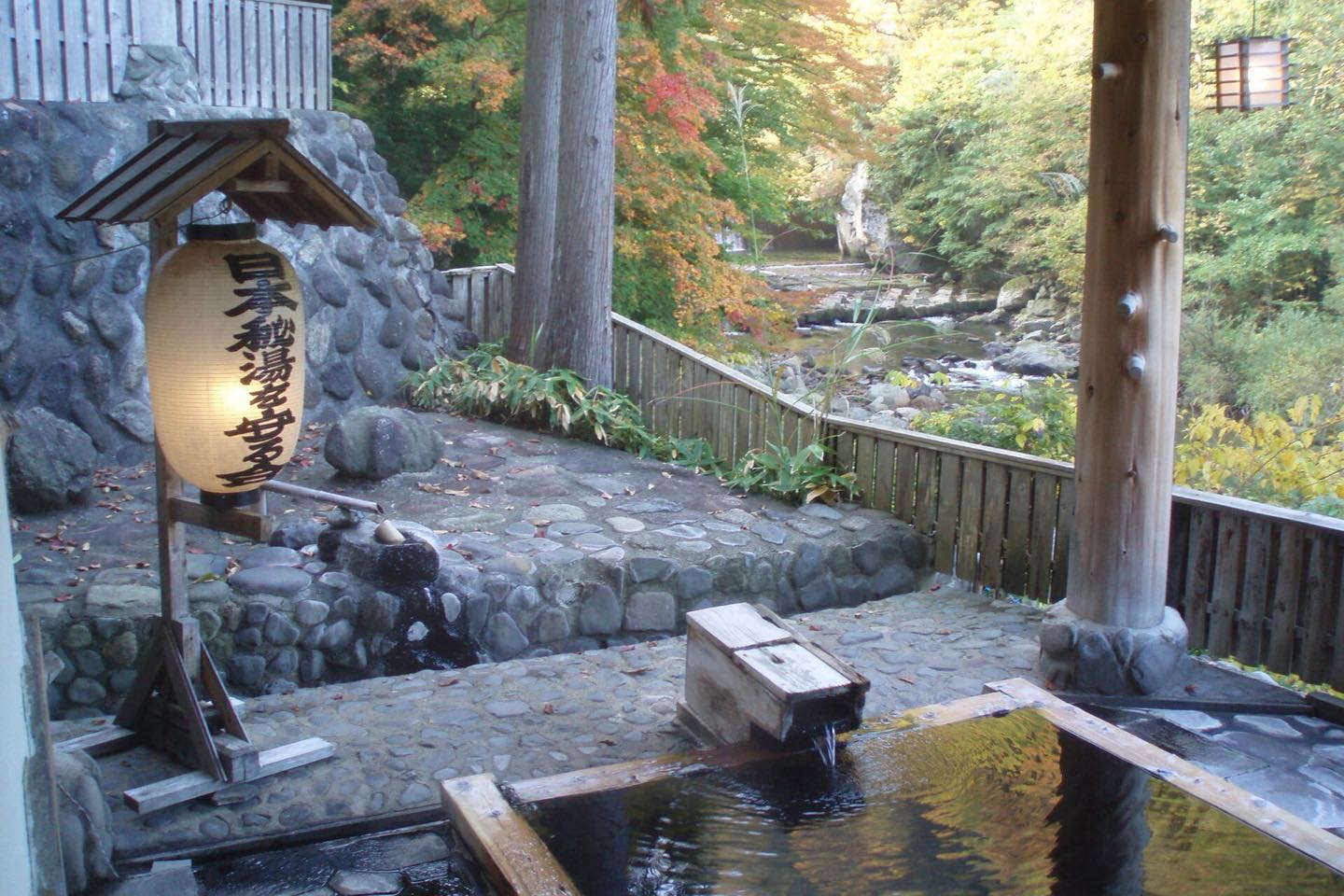 A lantern beside a stone outdoor hot-spring bath by a forest river