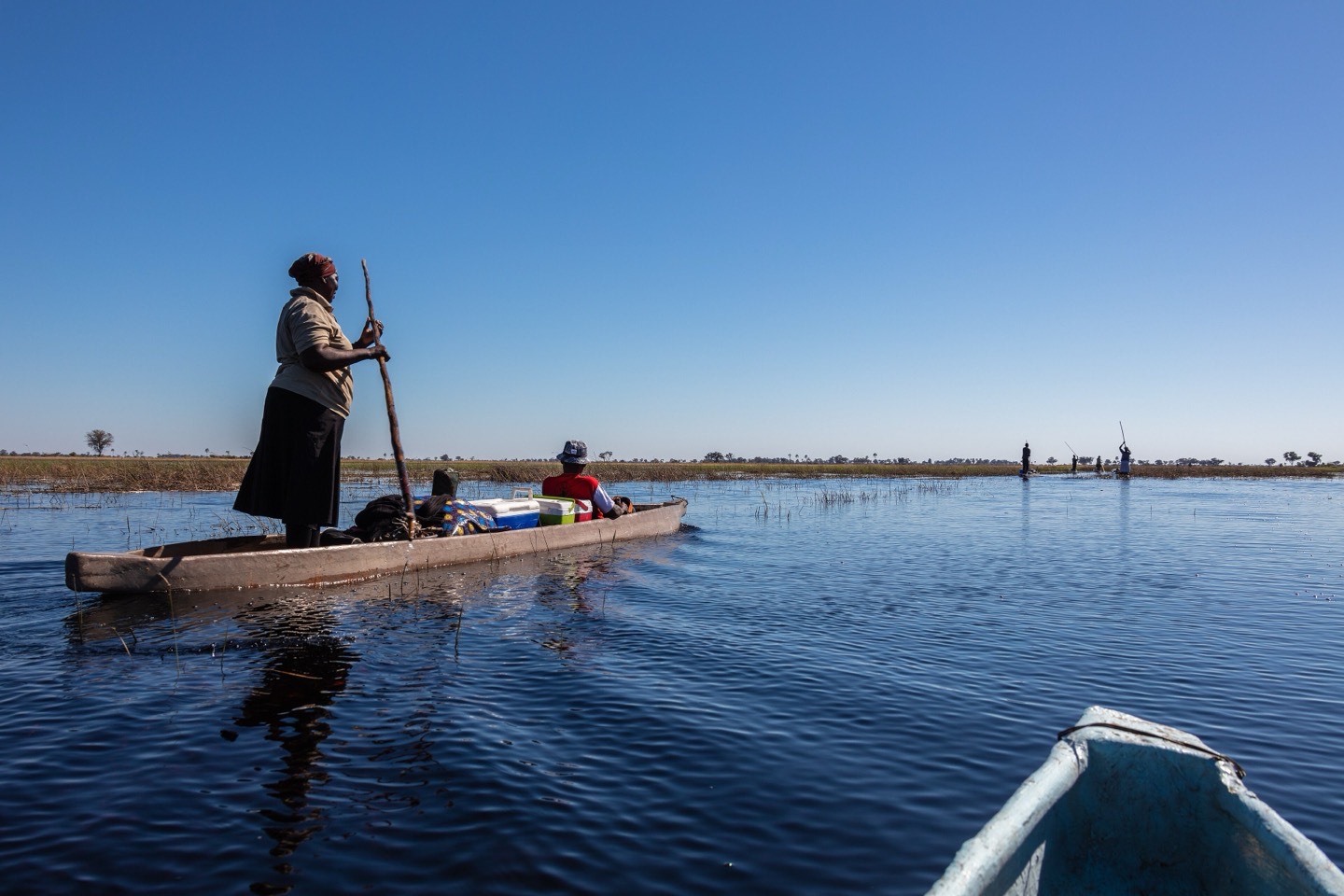 A poler standing in a wooden mokoro on open water in the Okavango Delta