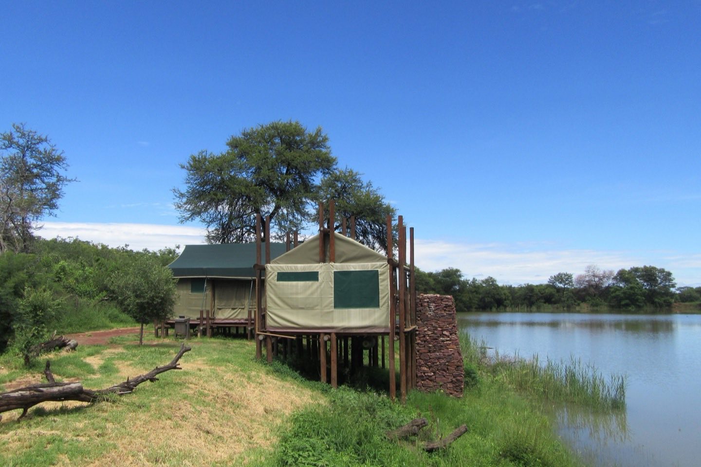Canvas safari tents on raised wooden decks beside a lake in the bush